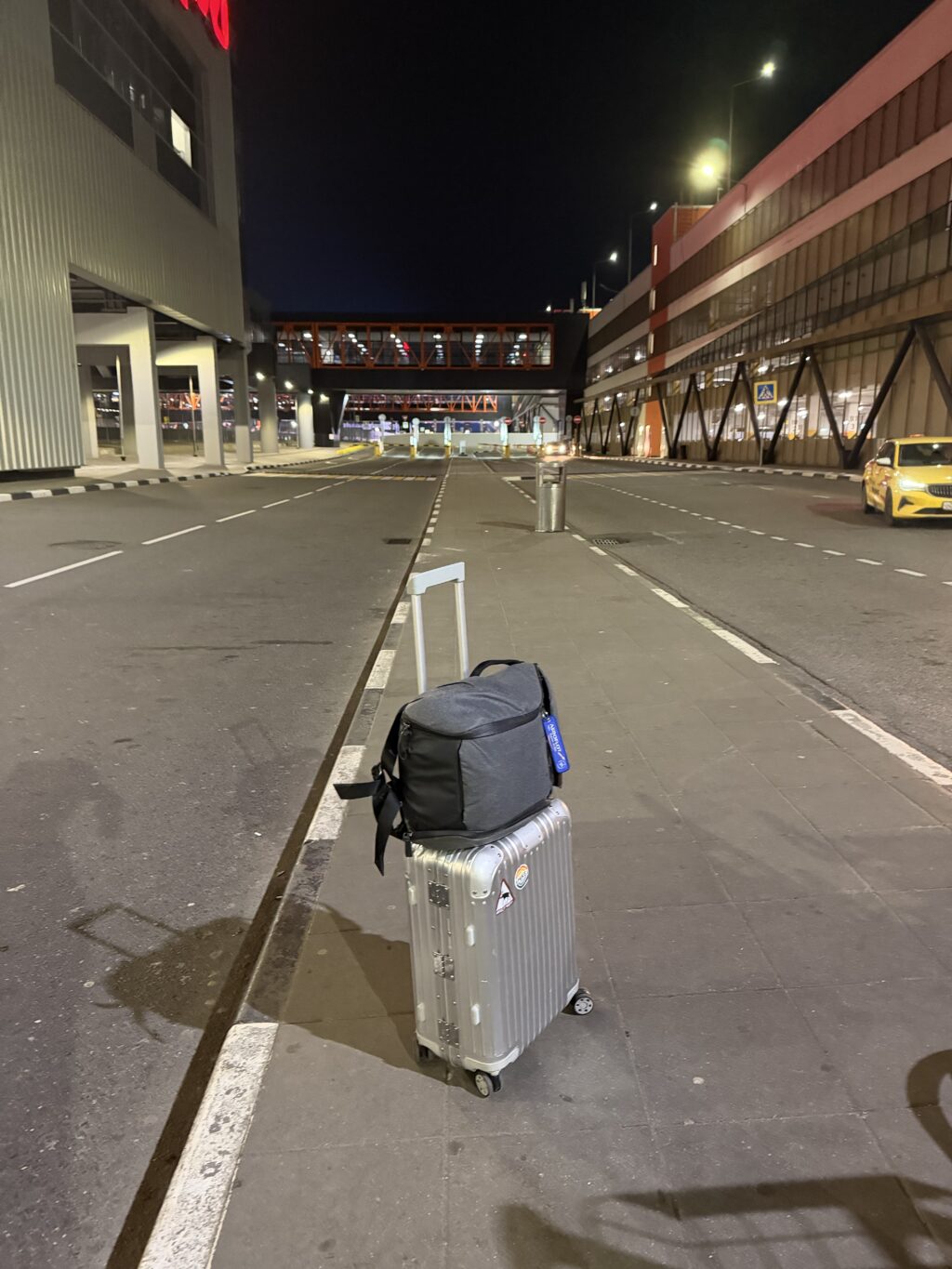 Серебристый чемодан Rimowa Cabin с ночью у терминала B аэропорта Шереметьево, ожидание трансфера на парковку Aero Parking в зоне высадки вылетающих пассажиров после рейса SU1117 из Краснодара